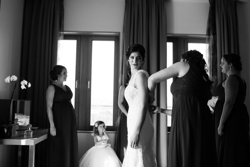 Classic black and white of bridesmaids helping bride button her dress