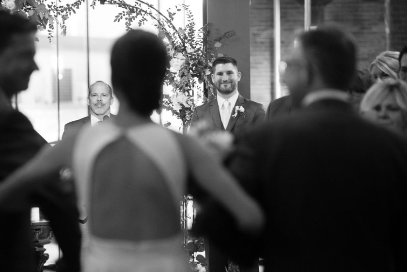 Groom smiling at his bride as she walks down the aisle at wedding ceremony at Heinz History Center Library